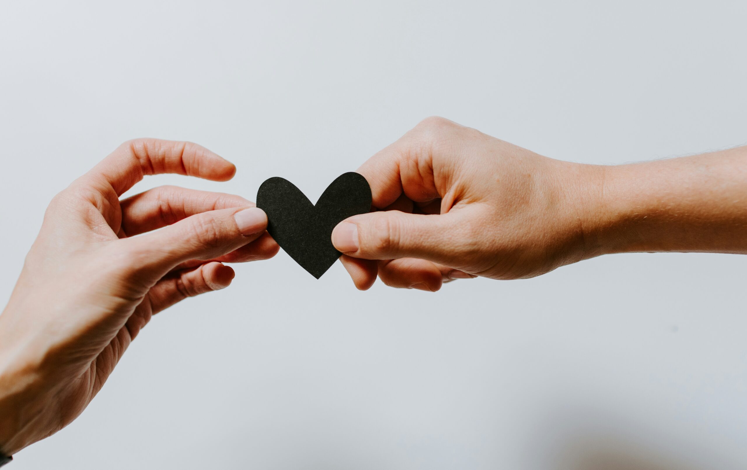 image of two hands reaching out to each other and holding a small paper love heart